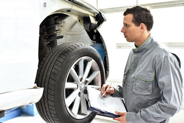 Mechaniker in autowerkstatt checkt Bremsen, Reifen und Fahrwerk mit Stossdämpfern eines Fahrzeuges
