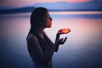 Beautiful woman lighted by candle in purple lake waters