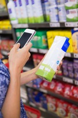 Woman comparing the price of a carton of milk with her phone