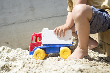 Young Boy Playing with his Plastic Truck Toy on White Sand