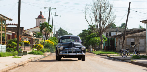 Kuba schwarzer Oldtimer fährt auf der Straße in Varadero mit einer Kirche im Hintergrund.