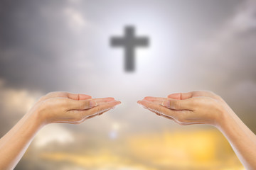 Hands of man praying over blurred the cross on the sky backgroun