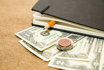 Naklejka premium notebook with a blank sheet pencil and money on the old tissue