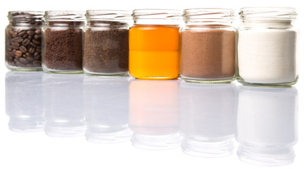 Coffee beans, coffee powder, creamer, cocoa powder, honey and processed tea leaves in a mason jar over white background