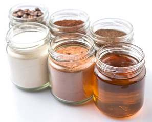 Coffee beans, coffee powder, creamer, cocoa powder, honey and processed tea leaves in a mason jar over white background