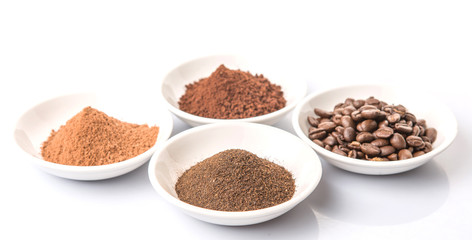 Coffee beans, powdered coffee, chocolate powder and processed tea leaves beverages in white bowl over white background