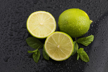 Green limes with mint and water drops on black background