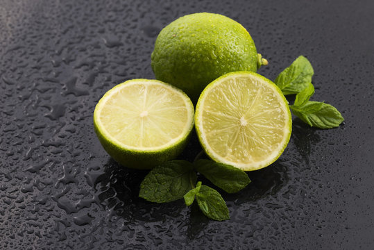 Green limes with mint and water drops on black background