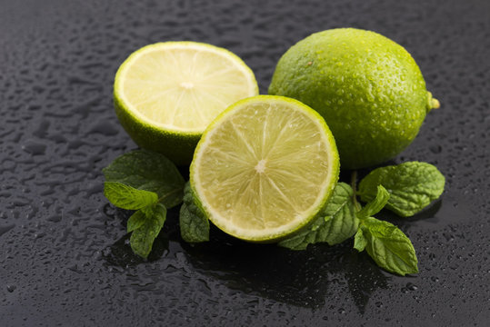 Green limes with mint and water drops on black background