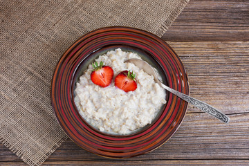 Oatmeal porridge topped with fresh strawberries on wooden table