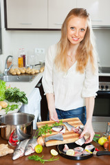  woman putting pieces of fish into fryingpan at  table