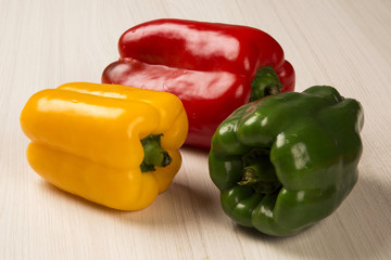 Some red, green and yellow peppers over a wooden surface