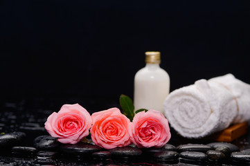 Fototapeta na wymiar Three rose and towel with massage oil and therapy stones 