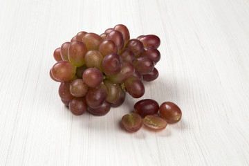 Some red grapes in a wooden pot over a wooden surface seen from