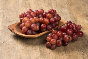 Some red grapes in a wooden pot over a wooden surface seen from