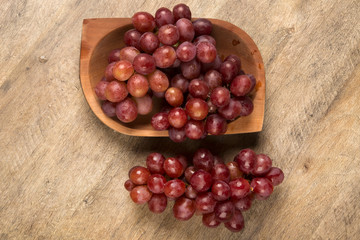 Some red grapes in a wooden pot over a wooden surface seen from