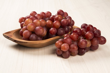 Some red grapes in a wooden pot over a wooden surface seen from