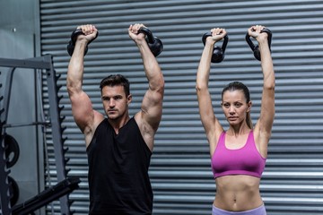 A muscular couple lifting kettlebells