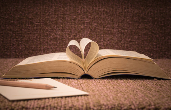 Pages of open book rolled in heart shape on table