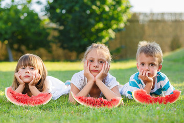 Bored little kids eating watermelon on the grass.