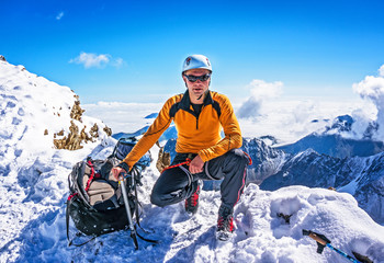 Climber on a mountain top posing on the background of snowy mountains