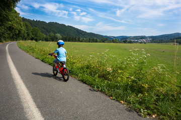 young boy with helmet riding his bike alone on cycling track to the city