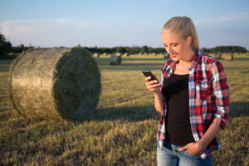 beautiful blonde woman with smart phone in field with haystacks