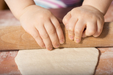 Detail of children hands kneading dough with wooden roller pin