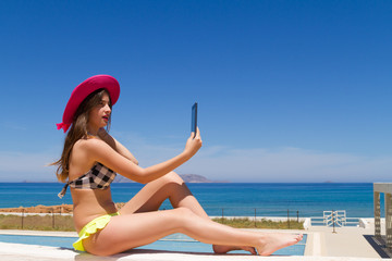 Brunette teen in swimwear enjoys the sun using her tablet.