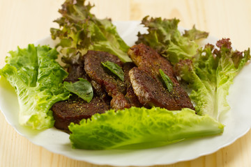 roast pork on white plate on wooden background with vegetables and herbs