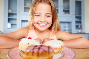 Young Girl Sitting At Table Looking At Plate Of Sugary Cakes