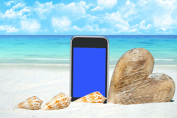 Smartphone, Herz aus Holz und Muscheln am Strand