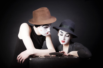 Two mimes in hats with a suitcase