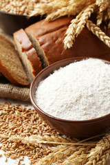 Ears of wheat and bowl of flour on white background