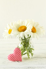 Chamomile flowers in vase on a white wooden background