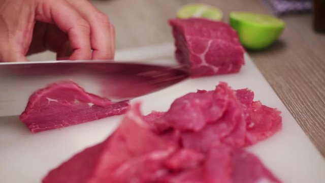 Chef finely slicing beef steak fillet using sharp knife, making beef carpaccio; close up;