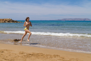 Fototapeta na wymiar Young busty brunette in swimwear jogging at the beach.