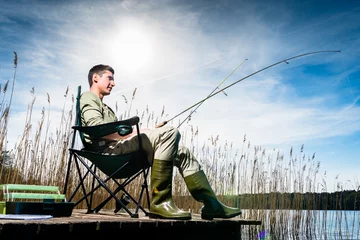 Foto auf Acrylglas Angeln Mann, der am See fischt, der auf Anlegestelle sitzt