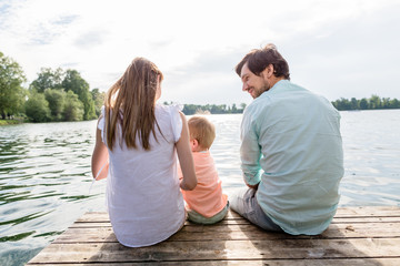 Familie sitzt auf Steg am See oder Teich