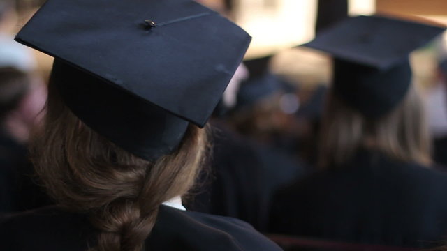 Young female in academic dress at diploma award ceremony, listening to lecture