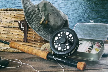 Poster Im Rahmen Hut- und Fliegenfischerausrüstung auf Tisch in der Nähe des Wassers © Sandra Cunningham