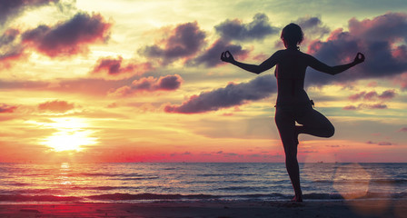 Woman doing meditation near the ocean beach. Yoga silhouette.