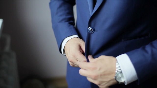 Buttoning a jacket. Stylish man in a suit fastening buttons on his jacket preparing to go out. Close up