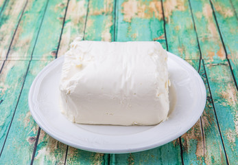 A block of cream cheese on a white plate over weathered wooden background