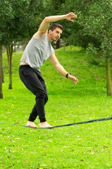 Man walking on slackline in park using arms to regain balance