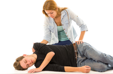 Couple demonstrating first aid techniques with male patient lying in recovery position and female sitting above him