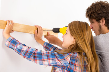 Couple renovating together as man using power drill on wooden plank being held up by woman