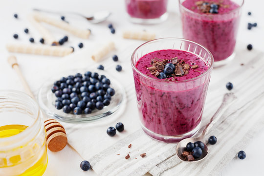 Fresh berry smoothie, milkshake, yogurt, dessert decorated grated chocolate, honey and blueberry on a white surface