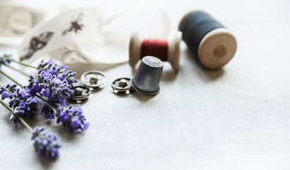 Obraz na płótnie Canvas Sewing tools with fresh lavander flowers on linen background. Vintage wooden spool, braid, thimble, buttons.