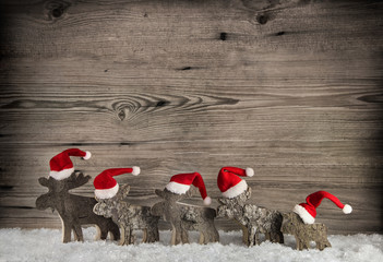 Geschnitze Elche oder Hirsche aus Holz mit Weihnachtsmützen auf Holz Hintergrund.